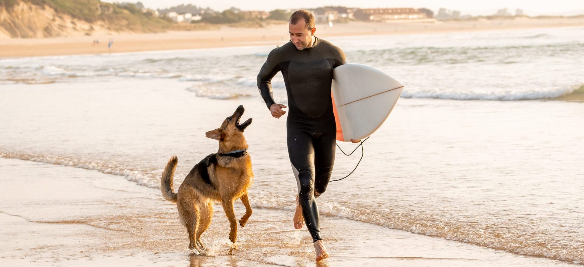 Surfer man with his dog german shepherd and surfboard playing and surfing on the beach
